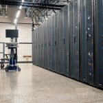 Gabinetes metálicos com servidores, equipamentos de rede e cabos em um data center moderno.