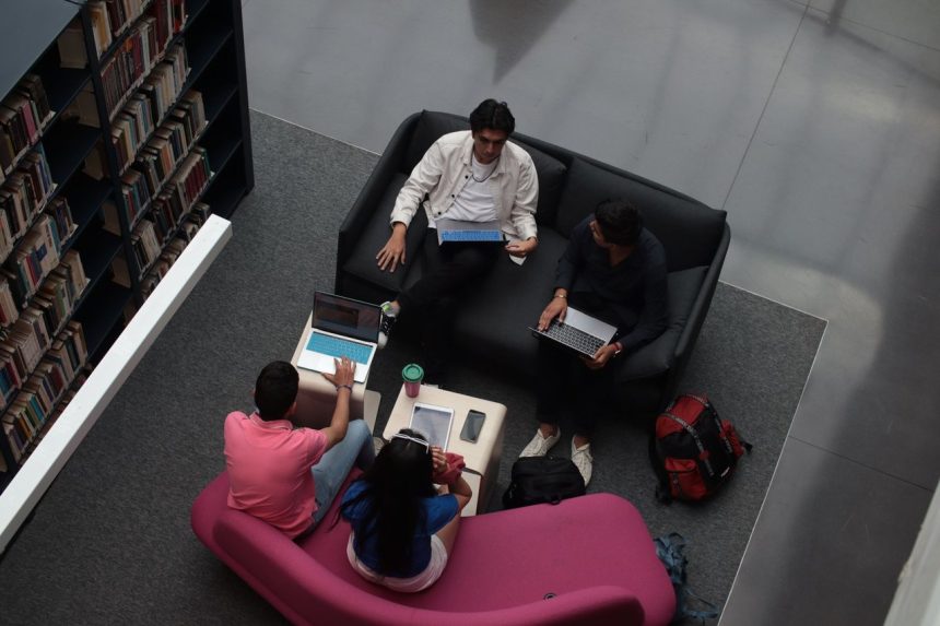 Grupo diverso de adultos colabora em laptops na área de convivência de uma biblioteca.