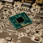 Close de um microchip montado em uma placa de circuito impresso, com componentes eletrônicos visíveis.