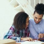 Mãe e filha estudam juntas em casa, usando um tablet como apoio à atividade.