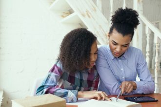 Mãe e filha estudam juntas em casa, usando um tablet como apoio à atividade.